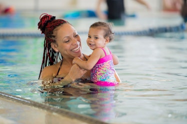 A mother holds her baby in a swimming pool.