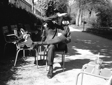 A black and white photograph of Christopher Niquet sitting on a chair in the shadow of a tree