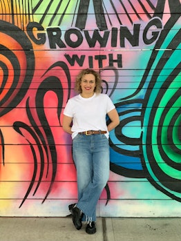 A curly-haired woman with a mural behind her