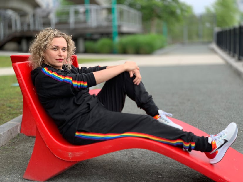 A curly-haired woman sitting on a red chair in a rainbow sweat suit