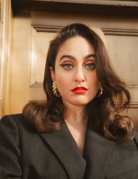 Comedian Catherine Cohen wearing a blazer, red lipstick and gold earrings.