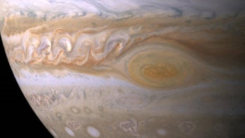 Color photo of Jupiter, with swirling red, orange, brown, and white clouds.