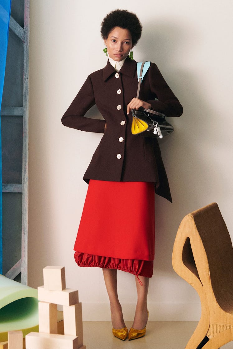A female model posing in a Tory Burch brown jacket and red skirt