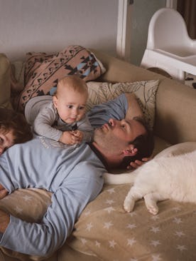 Man with two kids and a cat lying on the couch. 