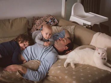 Man with two kids and a cat lying on the couch.