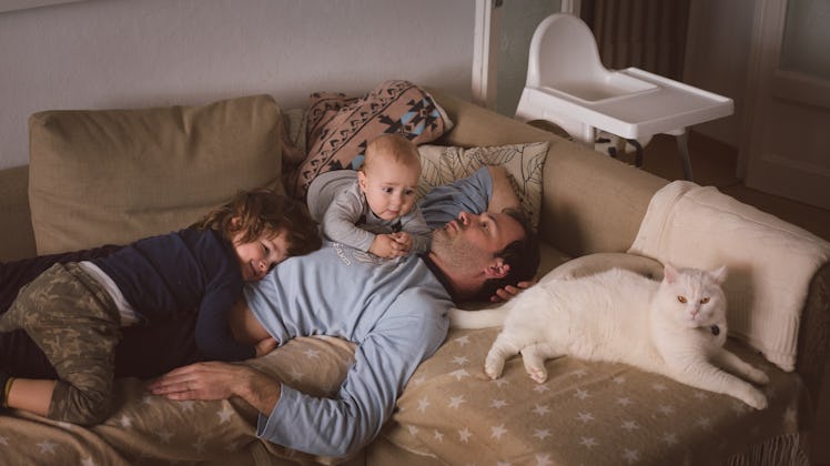 Man with two kids and a cat lying on the couch.