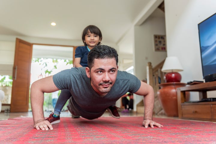 A man doing pushups in his living room while his son sits on his back