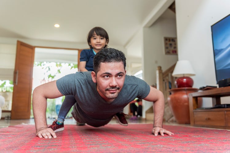 A man doing pushups in his living room while his son sits on his back