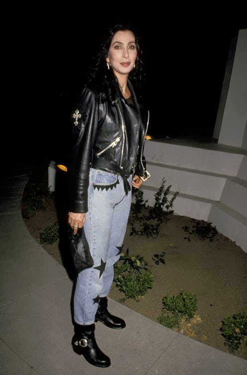 Woman in a stylish leather jacket and high-waisted jeans standing outside at night.