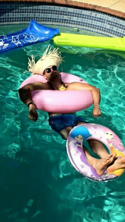 A man lying in a pool with a straw hat on while using two pink floaties