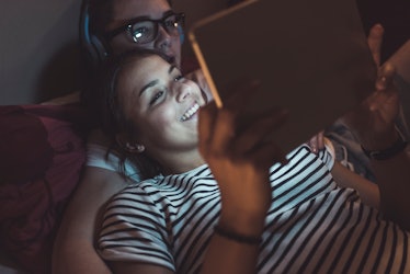 couple lying in bed watching their tablet together
