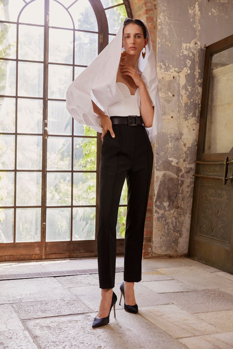 A model posing in a white Carolina Herrera top and black pants
