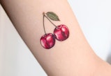 Bustle chatted with tattoo artist for summer 2022 tattoo trend predictions. Here, a small cherry tat...