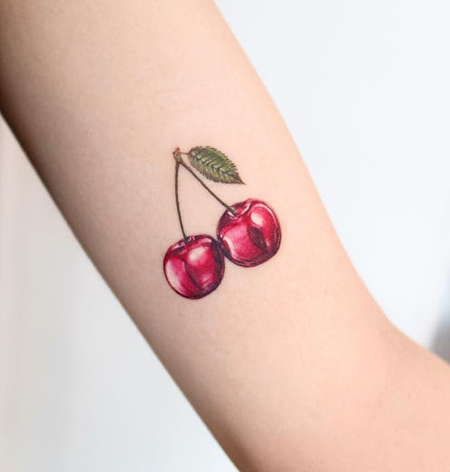Bustle chatted with tattoo artist for summer 2022 tattoo trend predictions. Here, a small cherry tat...