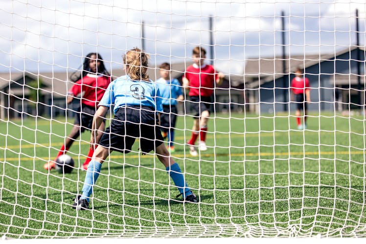 A soccer goalie defends against two opposing players who approach with the ball.