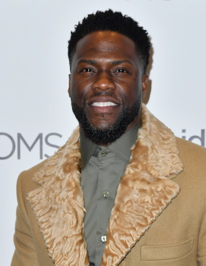Kevin Hart smiling for a photo with medium-length beard while wearing a brown coat