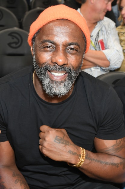 Idris Elba with medium-length beard posing in a black shirt