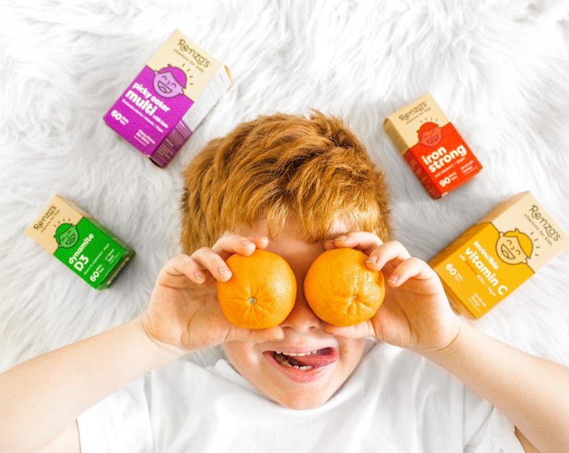 A picky eater boy placing two mandarins on his eyes with packages of vitamins spread on the floor ar...
