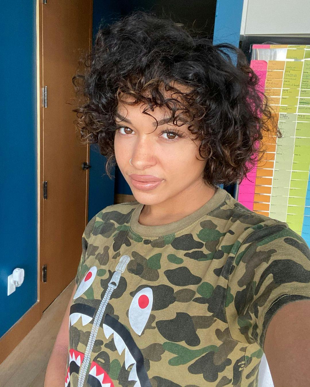 Princess Nokia wearing a camo shirt with a fake zipper and a monster face on it