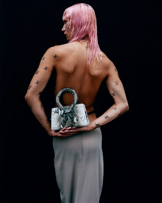 A pink-haired shirtless person holding a LUAR x Opening Ceremony bag