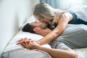 A couple kissing in bed as the woman pins down the man's hand.