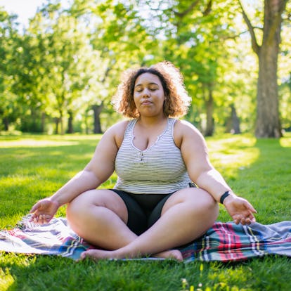 Young woman meditating on a picnic blanket during the July 2022 Super Buck Moon (aka the full moon i...