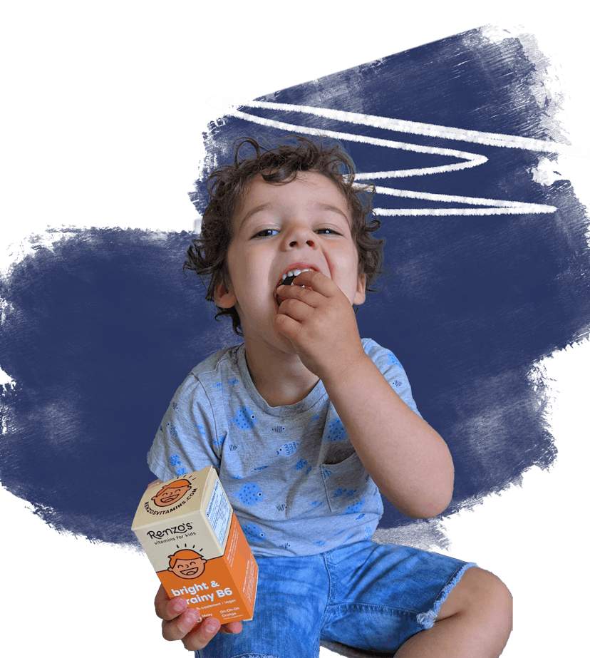 A toddler placing food in his mouth while holding the box of vitamins