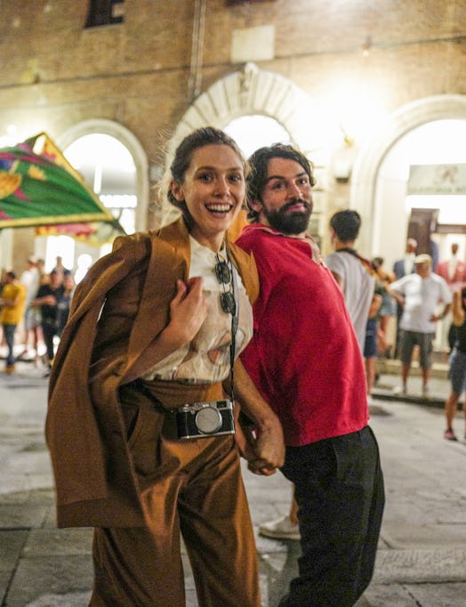 Elizabeth Olsen and Robbie Arnett holds hands in a public square at night.