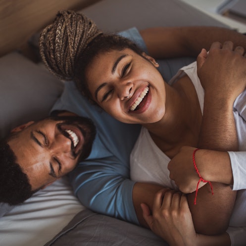 A wife and husband laughing in bed.