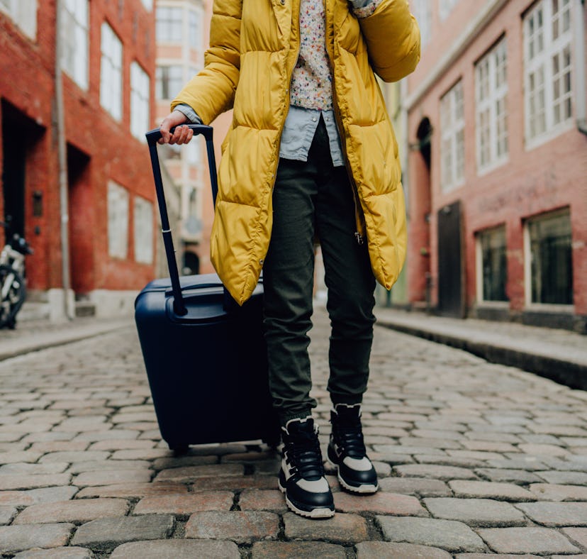 Young woman wheeling a suitcase she bought on Amazon Prime Day 2022, which has amazing deals on trav...