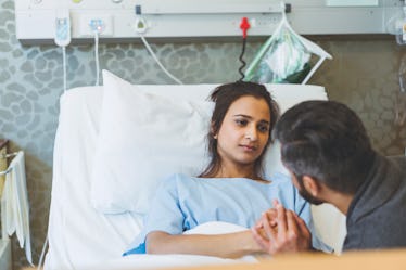 A sick woman in a hospital bed holding her husband's hand.