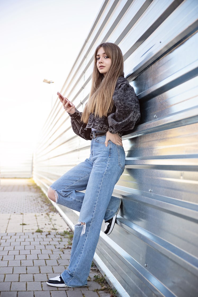 Young woman leaning against a wall holding her phone during the July 2022 full moon in Capricorn, wh...