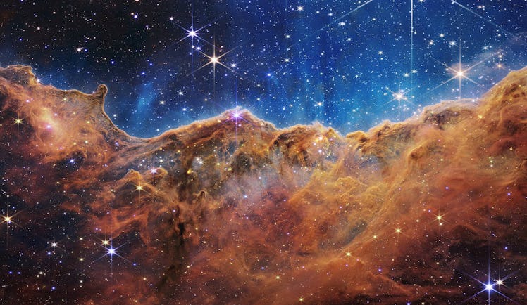 Color photo of brown and orange dust clouds against blue-lit space.