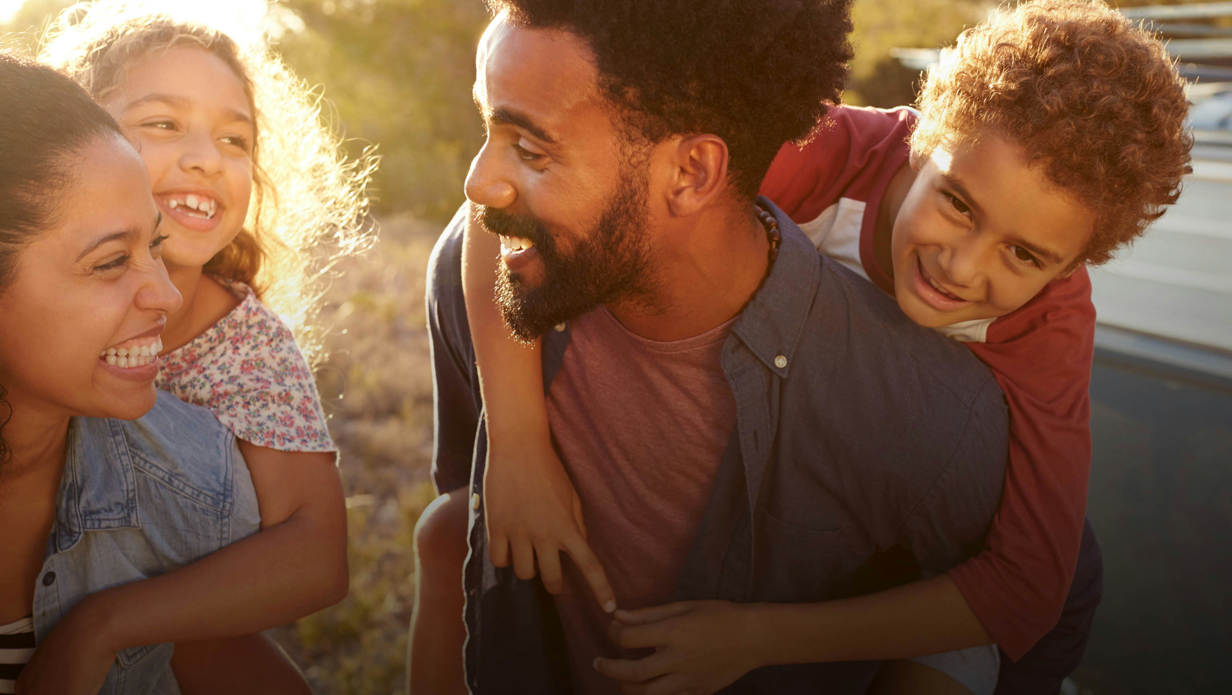 Two parents carrying their two kids on their backs and laughing