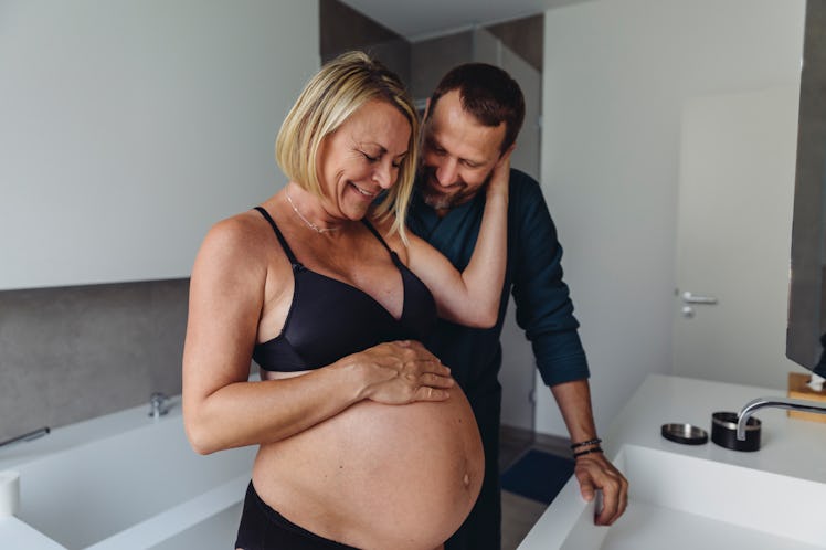 Woman with geriatric pregnancy standing with her husband, happily looking at her baby bump.
