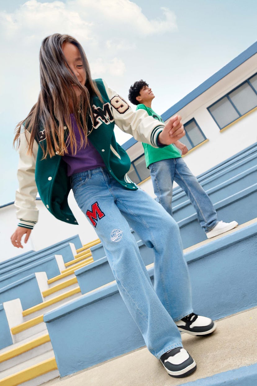 A girl wearing H&M's back-to-school college jacket and jeans and a boy wearing a green t-shirt and j...
