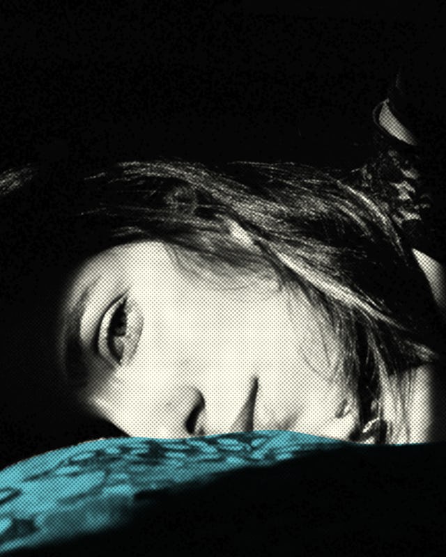 Face of a woman lying on her side and looking at the camera in black and white on a teal pillow