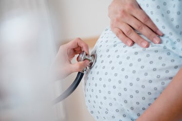 A doctor using a stethoscope on a pregnant person's baby bump.