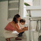 A child being potty trained sits on the toilet while mom kneels with him.