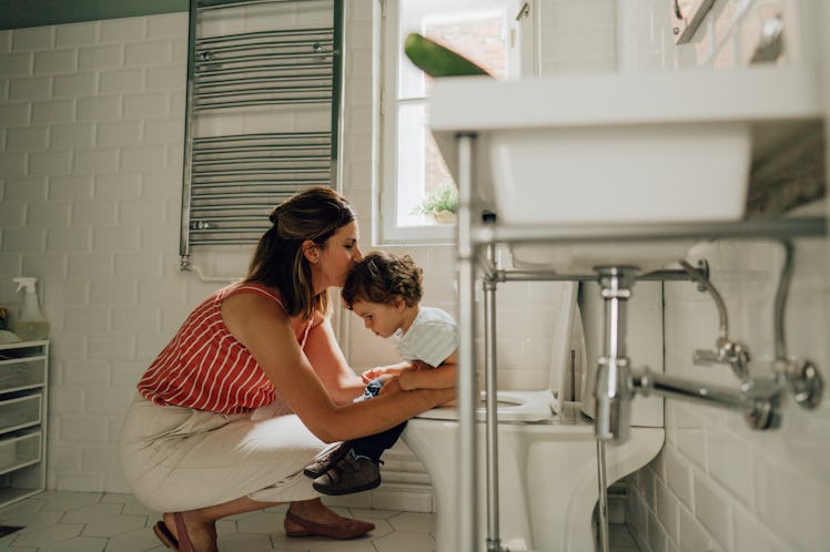 A child being potty trained sits on the toilet while mom kneels with him.