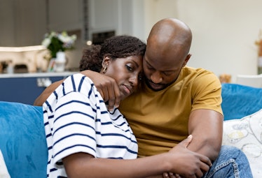A man comforts his sad wife after a miscarriage, holding her on the couch.