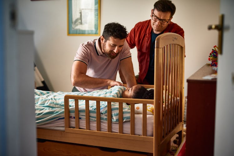Two dads tucking their young daughter into bed.