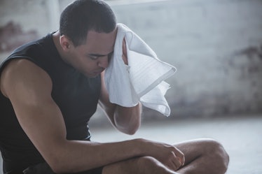 一名疲惫的男子在锻炼中坐下来，用毛巾擦干汗水。