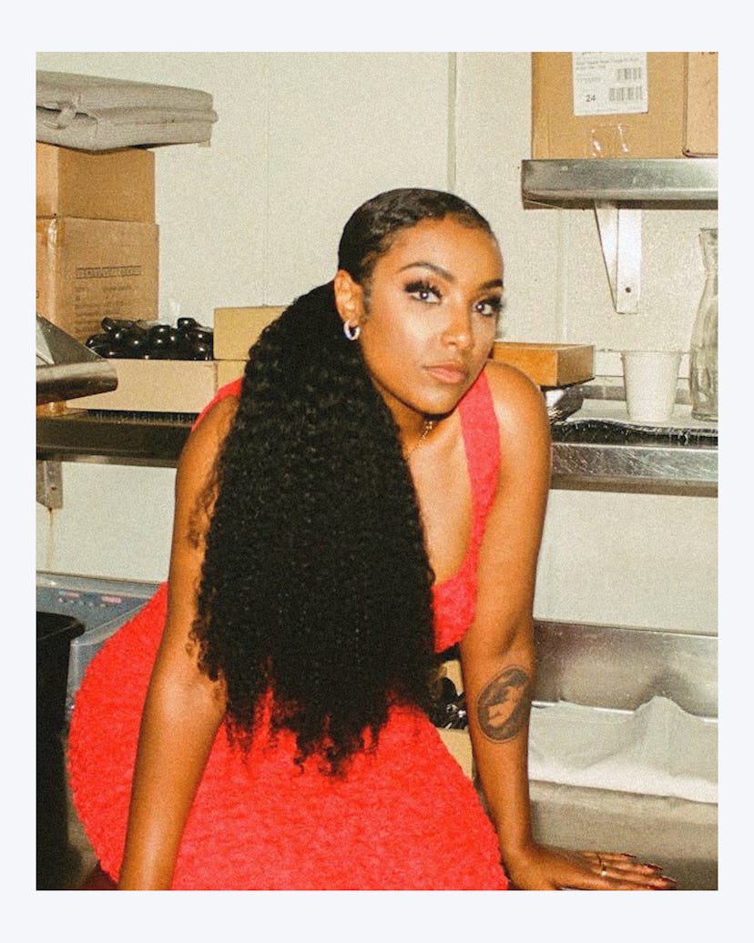 Aida Osman sitting in a film photo lab wearing a tight, bright red dress with hair styled in a low s...