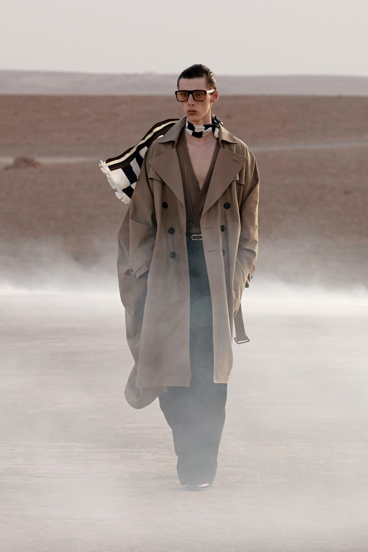 A model wearing a Saint Laurent brown trench coat and black and white scarf with sunglasses