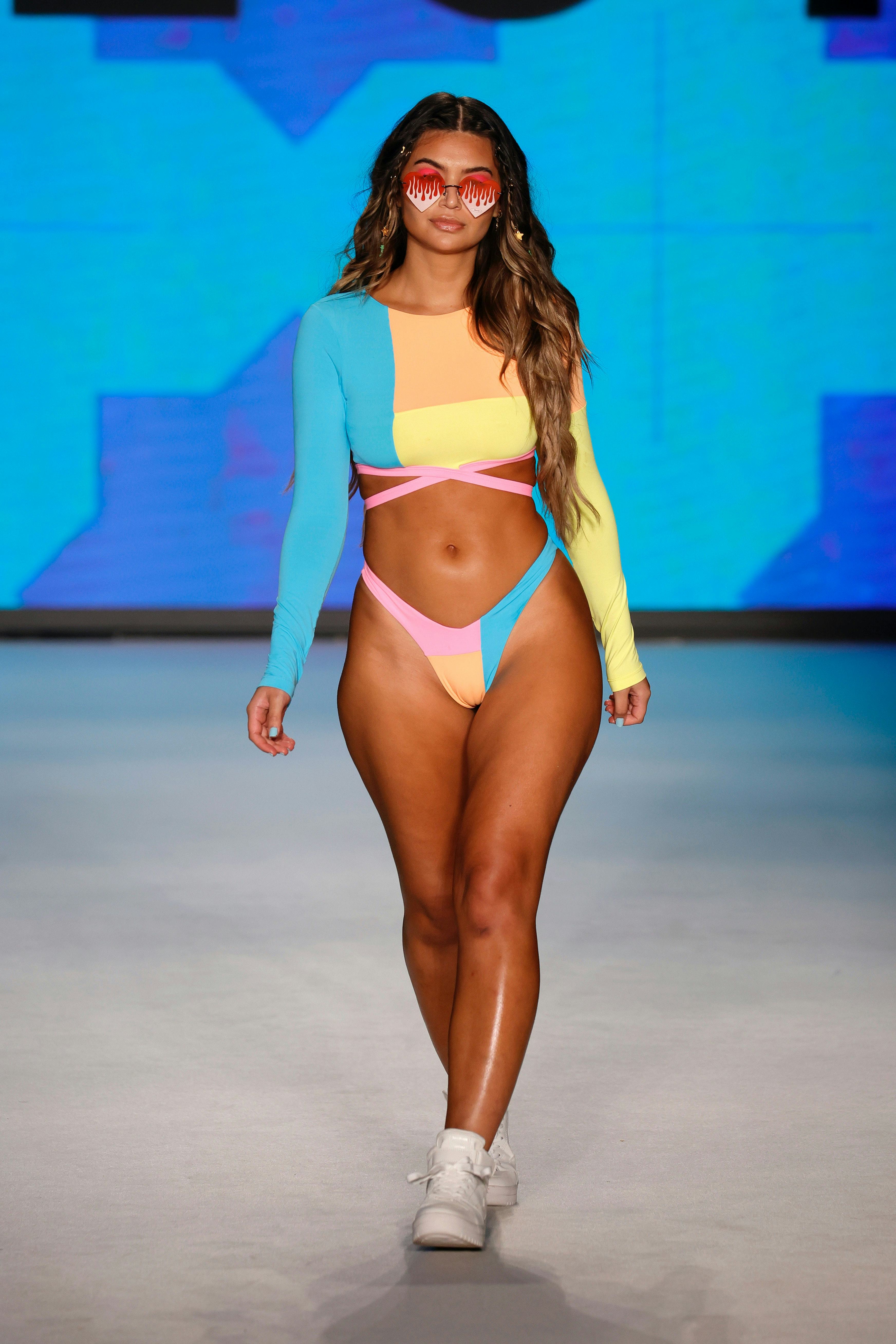 A young model walking in a blue, pink, orange, and yellow swimsuit at Paraiso Miami Beach Swim Week