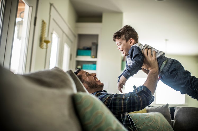 A dad on a couch holding his son in the air as they play.