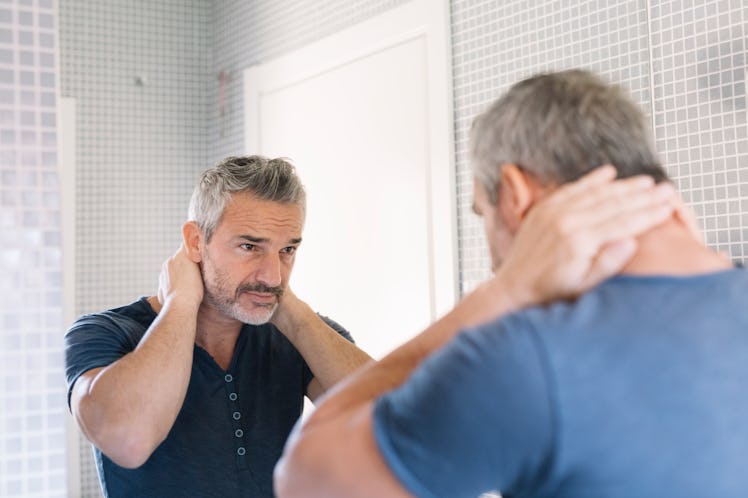 A stressed may with gray hair looks in the bathroom mirror.