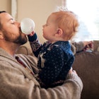 A dad blows a bubble with chewing gum while sitting on the couch and holding his son, who pokes at t...