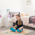 A girl practicing breathing exercises on the floor in her room.